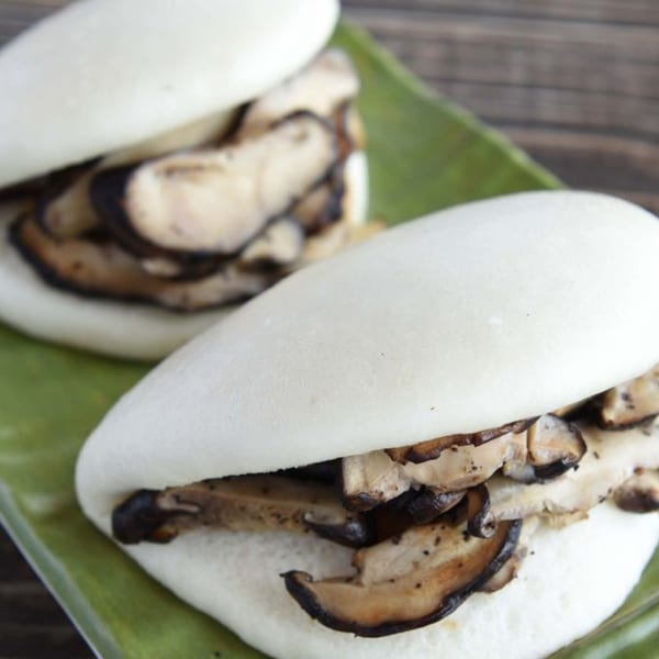 Two mushroom bao buns on a green plate, with a wooden background.