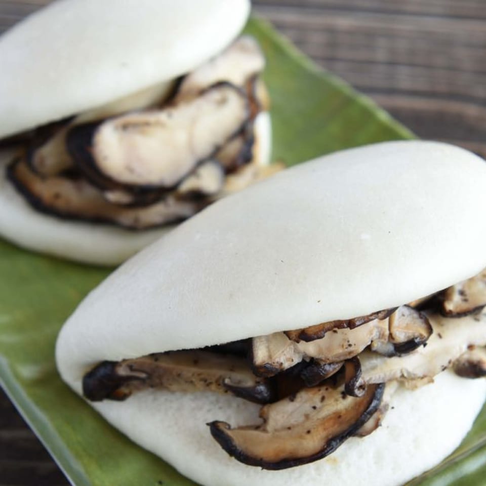 Two mushroom bao buns on a green plate, with a wooden background.