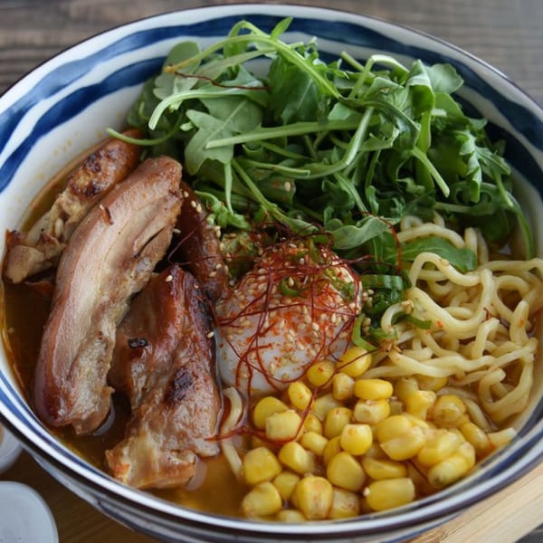 A bowl of Corner Ramen & Poke ramen with pork, corn, arugula, noodles, and a soft-boiled egg.