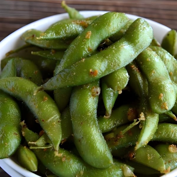 Close-up of a white bowl filled with vibrant green edamame pods, lightly seasoned.